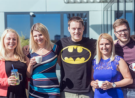 A group of employees are holding their shoulders around and posing for a photo