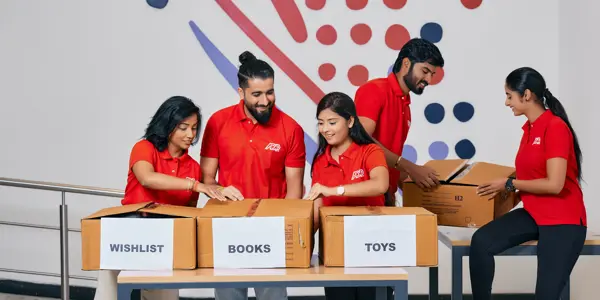 skupina lidí v červených košilích stojící kolem stolu s krabicemi